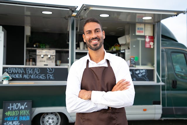 a man wearing an apron standing in front of a food truck